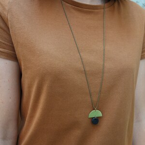 May include: A simple gold chain necklace with a green and black geometric pendant. The pendant is a half-circle shape with a smaller circle underneath.