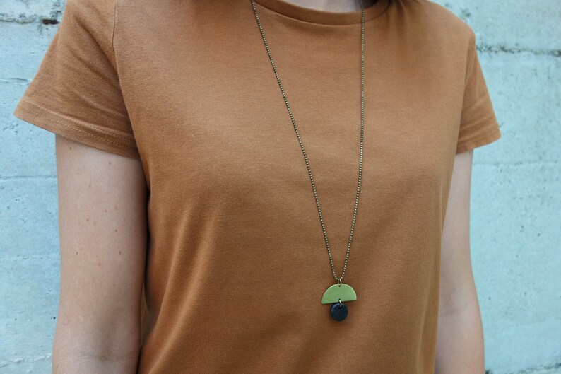 May include: A simple gold chain necklace with a green and black geometric pendant. The pendant is a half-circle shape with a smaller circle underneath.