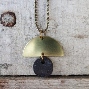 May include: A gold necklace with a half-circle pendant and a black round pendant.