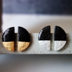 Puede incluir: Un par de pendientes de medio círculo negro y blanco con detalles dorados y plateados. Los pendientes están hechos de un material moteado.