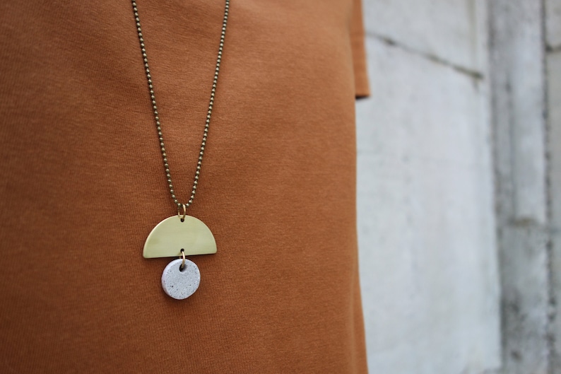May include: A gold chain necklace with a brass half-circle pendant and a small white speckled circle pendant.