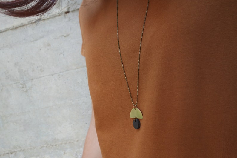 May include: A gold necklace with a black and gold pendant. The pendant is a half circle shape with a smaller circle hanging from it.
