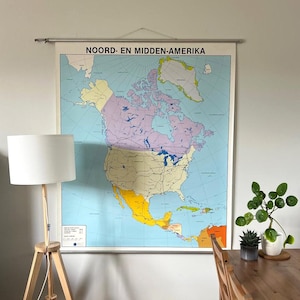 Op de afbeelding: Een vintage kaart van Noord-Amerika, getiteld "NOORD- EN MIDDEN-AMERIKA". De kaart is kleurgecodeerd met blauw, geel, paars en groen. Hij is gemonteerd op een houten staaf.