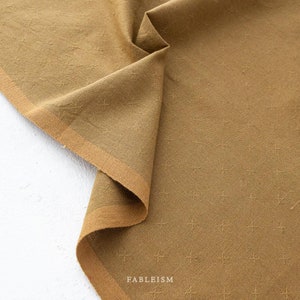 May include: A close-up of a brown fabric with a subtle cross-stitch pattern. The fabric is folded and the edge is visible. The text "FABLEISM" is printed on the fabric.