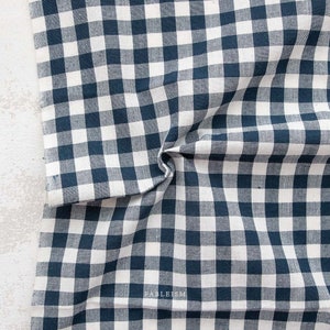 May include: A white and navy blue gingham fabric with a checkered pattern. The fabric is folded and has a slight wrinkle.