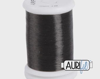 May include: A spool of dark gray thread with a white top and base. The thread is labeled "AURIFIL" and "100% NYLON MADE IN ITALY". The spool is cylindrical and appears to be full of thread.
