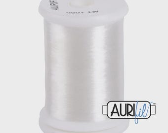 May include: A white spool of Aurifil thread, made in Italy. The spool is labeled "100% Nylon" and "MT 1000". The Aurifil logo is visible on the side. This thread is likely used for sewing, quilting, or embroidery projects.