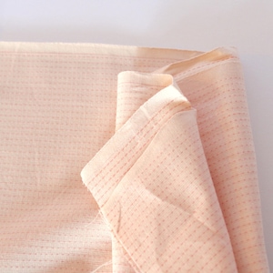 May include: Close-up of a folded piece of peach-colored fabric. The fabric has a textured, dotted pattern and visible stitching. The edges are neatly finished, suggesting a textile or craft material.