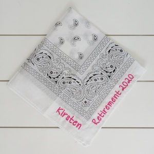 May include: White bandana with a black paisley pattern and pink embroidery that reads "Kirsten Retirement 2020".