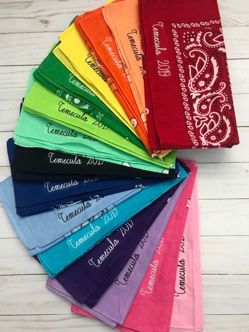 May include: A stack of colorful bandanas with the word "Temecula" and a year embroidered on each one. The bandanas are arranged in a fan shape, with the top bandana being red with a paisley pattern.