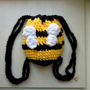 May include: A small yellow and black crocheted bee-shaped drawstring bag with white crocheted wings.