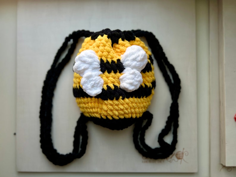 May include: A small yellow and black crocheted bee-shaped drawstring bag with white crocheted wings.