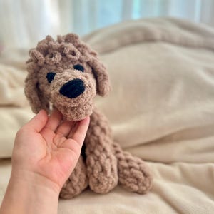 Pode incluir: Um c&atilde;o de pel&uacute;cia feito &agrave; m&atilde;o, em tons de castanho. O c&atilde;o tem um design texturizado e em la&ccedil;o, com nariz e olhos pretos. O brinquedo foi projetado para se assemelhar a um poodle. O c&atilde;o est&aacute; sentado em uma superf&iacute;cie bege macia.