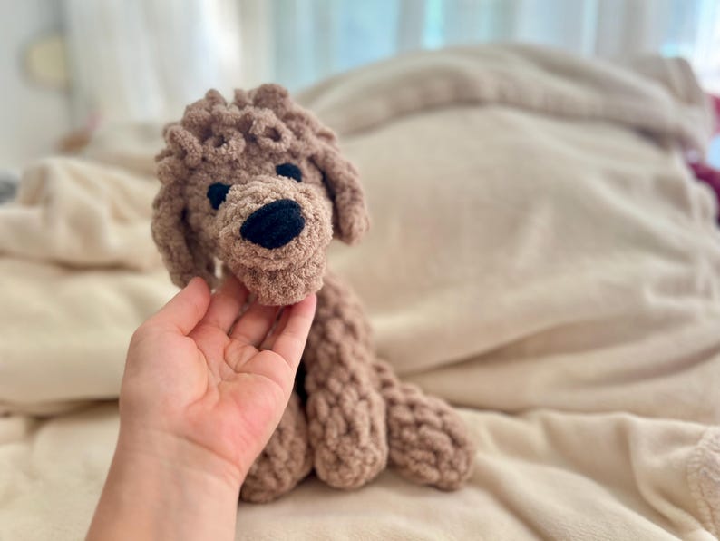 Pode incluir: Um c&atilde;o de pel&uacute;cia feito &agrave; m&atilde;o, em tons de castanho. O c&atilde;o tem um design texturizado e em la&ccedil;o, com nariz e olhos pretos. O brinquedo foi projetado para se assemelhar a um poodle. O c&atilde;o est&aacute; sentado em uma superf&iacute;cie bege macia.