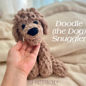 Pode incluir: Um brinquedo de cachorro de croch&ecirc; marrom feito &agrave; m&atilde;o com nariz e olhos pretos. O texto "Doodle (the Dog) Snuggler" &eacute; exibido no lado direito da imagem. As palavras "PDF PATTERN ONLY" est&atilde;o na parte inferior.