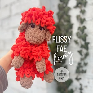 May include: A handmade crochet sheep toy with bright red curly wool and a brown face, ears, and hooves. The text "FLISSY FAE Lovey" is visible on the right side of the image, along with "PDF PATTERN ONLY".