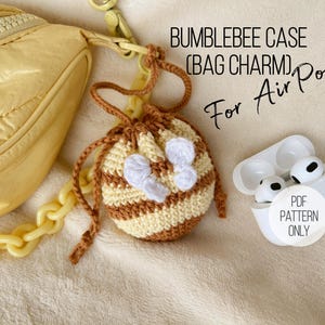 May include: A crocheted bumblebee-themed bag charm for AirPods. The charm is yellow and brown with white accents, and is next to a yellow purse and a white AirPods case. Text on the image reads "BUMBLEBEE CASE (BAG CHARM) For AirPods PDF PATTERN ONLY."