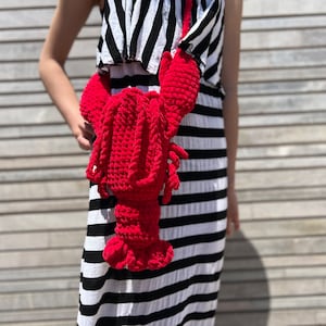 May include: A red crocheted lobster bag worn as a crossbody bag by a person wearing a black and white striped dress.