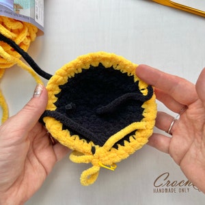 May include: A close-up of a crocheted yellow and black circle with a black center. The circle is being held by two hands, and the yellow yarn is being pulled through the center.