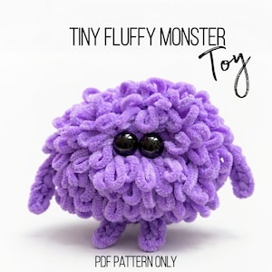 Può includere: Un giocattolo mostro viola soffice fatto a mano con occhi a bottone neri. Il giocattolo ha braccia e gambe piccole ed è fatto di un filato morbido e ad anello. Il testo sull'immagine recita "Tiny Fluffy Monster Toy" e "PDF Pattern Only".