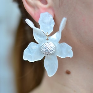 May include: White flower-shaped earrings with a sparkly rhinestone center.