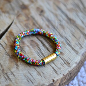 May include: A colourful beaded bracelet with a gold clasp. The bracelet is made of small, multi-coloured beads and is a vibrant and eye-catching piece of jewellery.