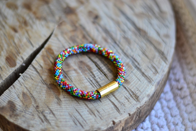May include: A colourful beaded bracelet with a gold clasp. The bracelet is made of small, multi-coloured beads and is a vibrant and eye-catching piece of jewellery.