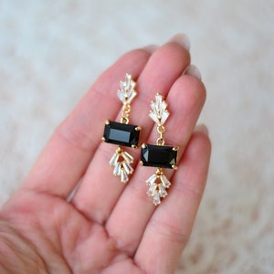 May include: A pair of gold earrings with black rectangular stones and clear crystal accents.