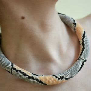 May include: A beaded necklace in the shape of a snake, with black, white and peach coloured beads.