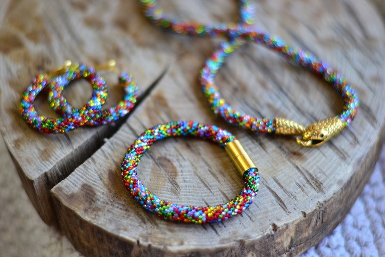 May include: A set of colourful beaded jewellery, including a necklace, bracelet, and earrings. The jewellery is made with small, multi-coloured beads and features gold accents.