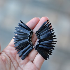 May include: A pair of black earrings with a fan-shaped design. The earrings are made of black feathers and have a black bead detail.