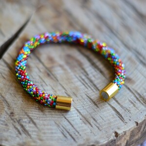 May include: A colourful beaded bracelet with gold magnetic clasps. The bracelet is made of small, colourful beads that are woven together in a pattern. The bracelet is a great accessory for any outfit.