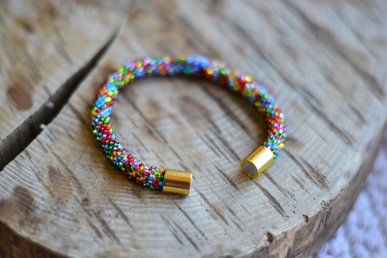 May include: A colourful beaded bracelet with gold magnetic clasps. The bracelet is made of small, colourful beads that are woven together in a pattern. The bracelet is a great accessory for any outfit.