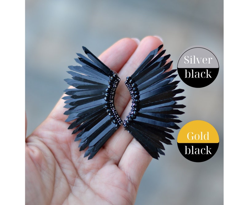 May include: A pair of black earrings with a feather-like design. The earrings are made of black feathers and have a silver or gold base.