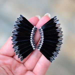 May include: A pair of black and silver earrings with a fan-like design. The earrings are made of small, flat pieces of metal that are arranged in a fan shape. The earrings are accented with small, silver beads.