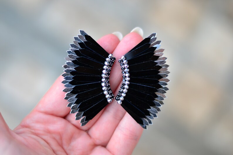 May include: A pair of black and silver earrings with a fan-like design. The earrings are made of small, flat pieces of metal that are arranged in a fan shape. The earrings are accented with small, silver beads.