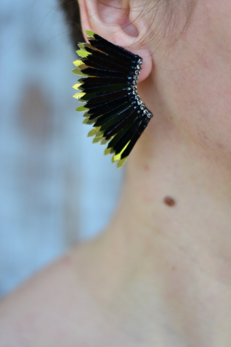 May include: A pair of black and gold earrings with a fan-like design. The earrings are made of metal and have a geometric shape.