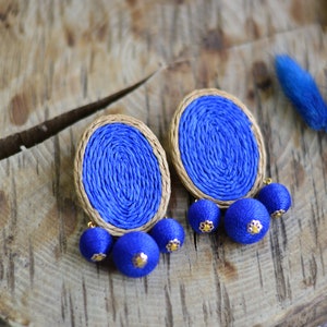 May include: A pair of blue and brown oval earrings with three blue tassel charms hanging from each earring.