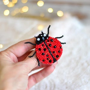 May include: A red and black beaded ladybug brooch. The ladybug has black spots and white eyes.
