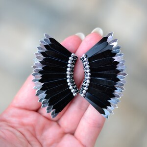 May include: A pair of black and silver earrings with a fan-like design. The earrings are made of small, black and silver beads that are arranged in a fan shape. The earrings are held together by a silver wire.