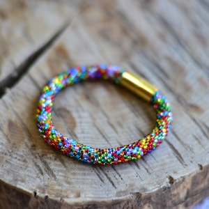 May include: A colourful beaded bracelet with a gold clasp. The bracelet is made of small, multi-coloured beads and is woven in a tight pattern.
