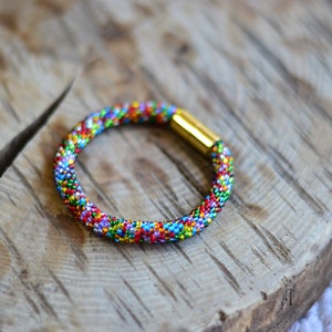 May include: A colourful beaded bracelet with a gold clasp. The bracelet is made of small, multi-coloured beads and is a great accessory for any outfit.