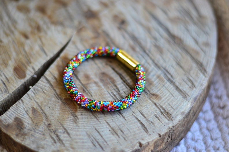 May include: A colourful beaded bracelet with a gold clasp. The bracelet is made of small, multi-coloured beads and is a great accessory for any outfit.
