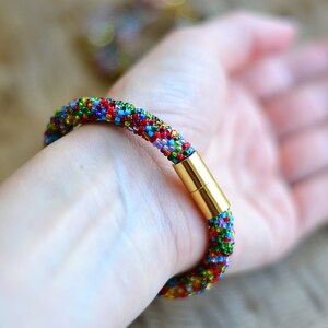 May include: A colourful beaded bracelet with a gold magnetic clasp. The bracelet is made of small, multi-coloured beads and is worn on a person's wrist.