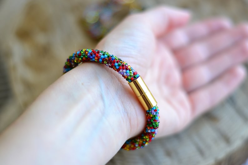 May include: A colourful beaded bracelet with a gold magnetic clasp. The bracelet is made of small, multi-coloured beads and is worn on a person's wrist.