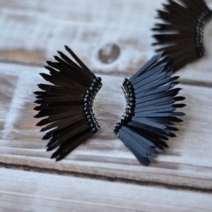 May include: A pair of black feather earrings with a black bead detail. The earrings are shaped like a fan and are made of many small feathers.