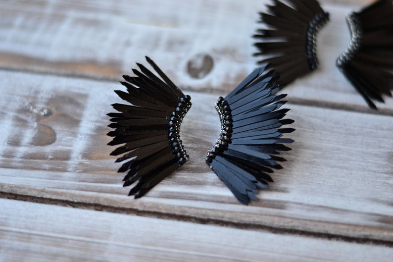 May include: A pair of black feather earrings with a black bead detail. The earrings are shaped like a fan and are made of many small feathers.