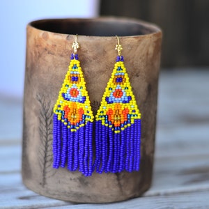May include: A pair of long, beaded earrings with a yellow, blue, and orange geometric pattern and purple fringe.