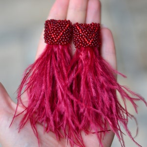 May include: A pair of red feather earrings with a beaded top. The earrings are long and dangle.