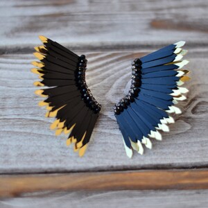 May include: A pair of black and gold earrings with a fan-shaped design. The earrings are made of black feathers with gold tips.